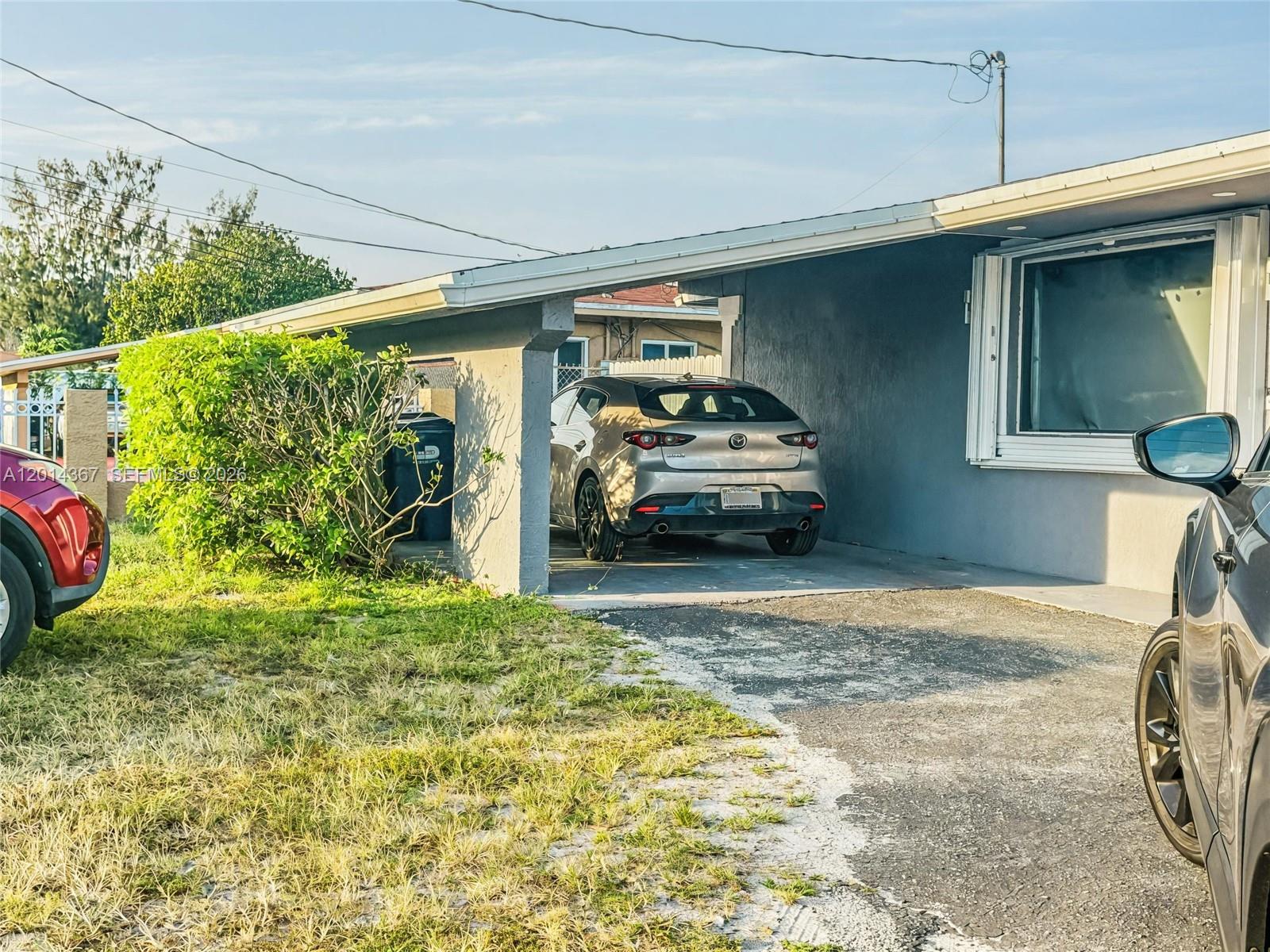 A beige Mazda hatchback is parked under a carport attached to a gray house — 18901 NW 28th Pl, Miami Gardens FL 33056, MIAMI GARDENS, FL