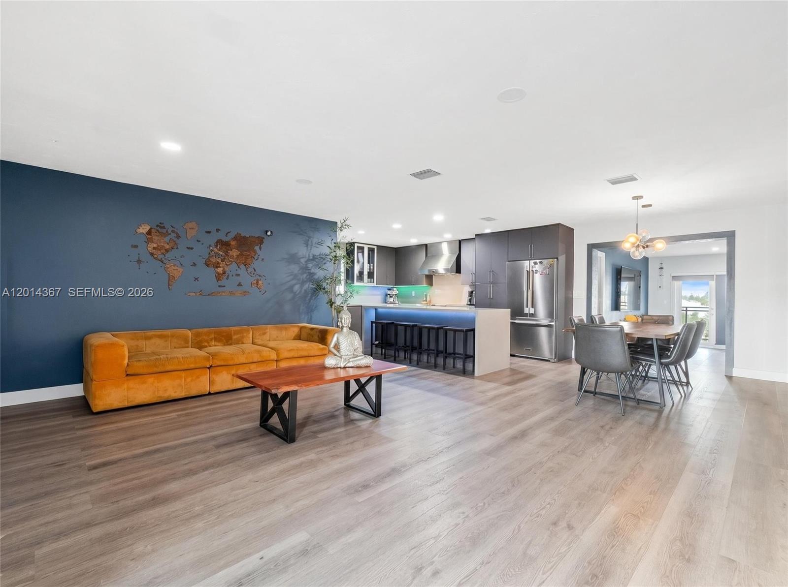 An open-concept living room and kitchen feature a blue accent wall and wood flooring — 18901 NW 28th Pl, Miami Gardens FL 33056, MIAMI GARDENS, FL