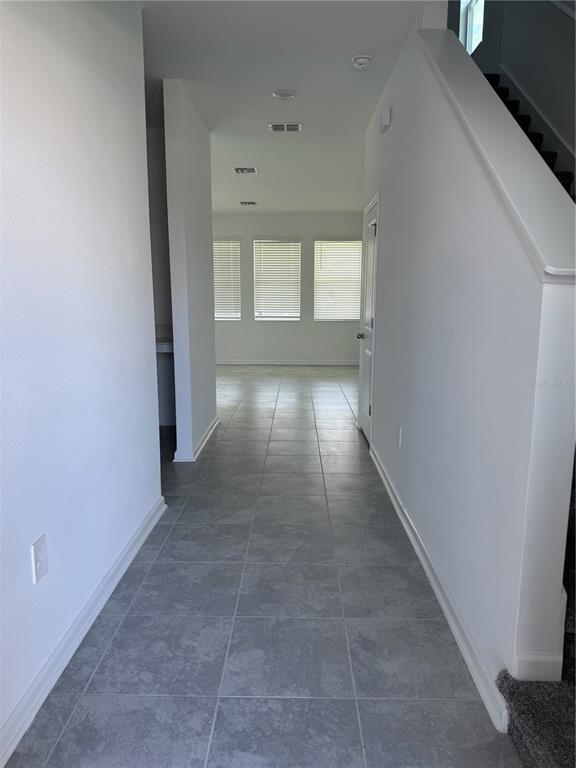 A hallway with gray tile flooring leads toward a room with three windows — 1952 ROCK MAPLE BEND, KISSIMMEE, FL