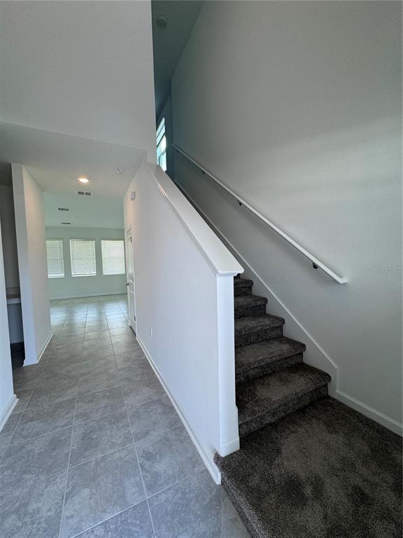 A carpeted staircase with a white handrail sits beside a tiled hallway leading to windows — 1952 ROCK MAPLE BEND, KISSIMMEE, FL