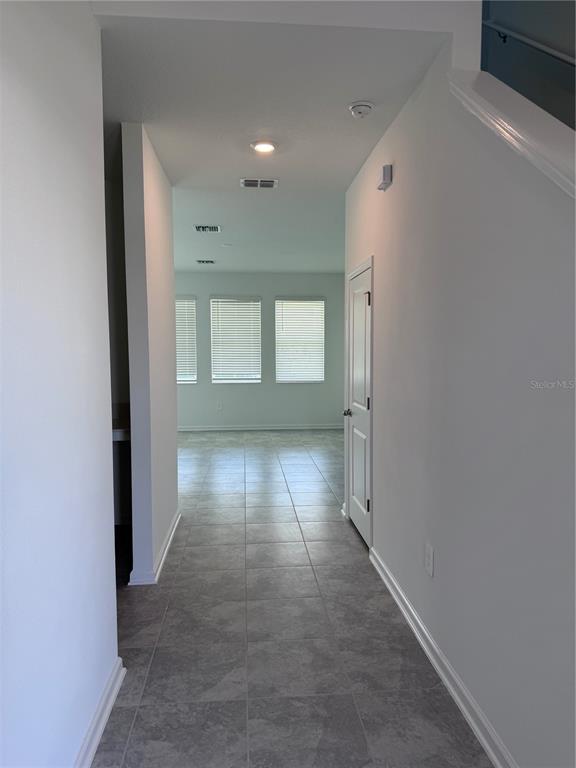 A hallway with gray tile flooring leads to an open living area with three windows — 1952 ROCK MAPLE BEND, KISSIMMEE, FL