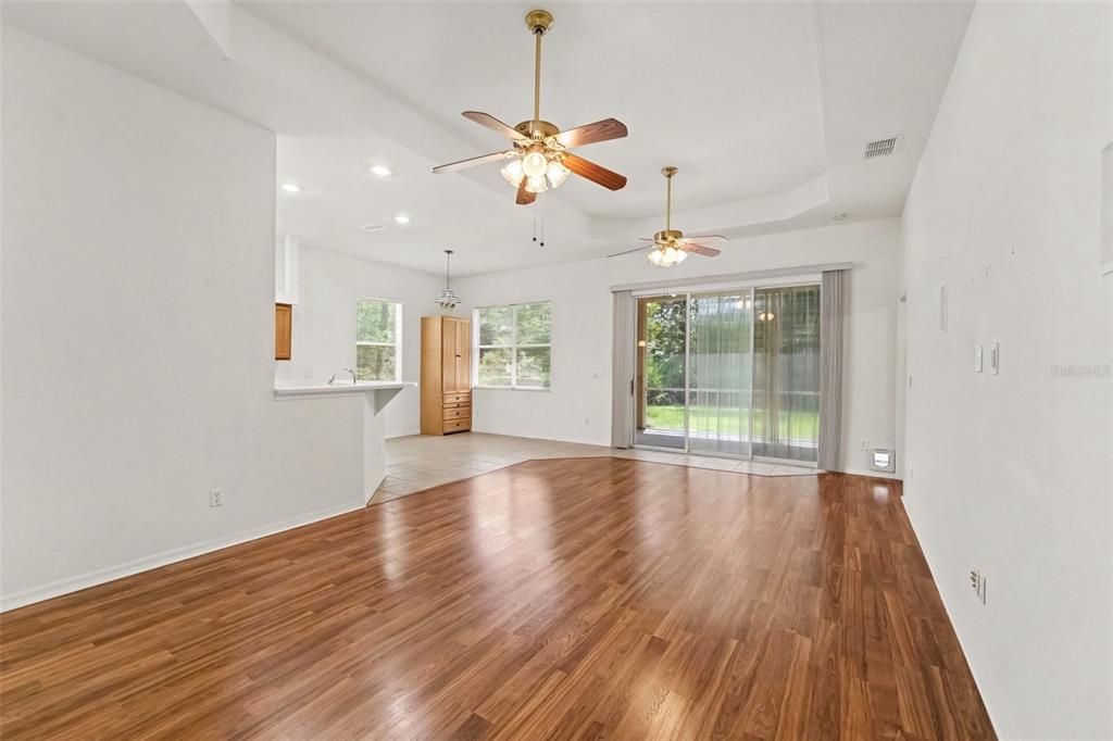 A spacious living room with wood-look flooring, a tray ceiling, and sliding glass patio doors — 48 CACTUS STREET, HOMOSASSA, FL