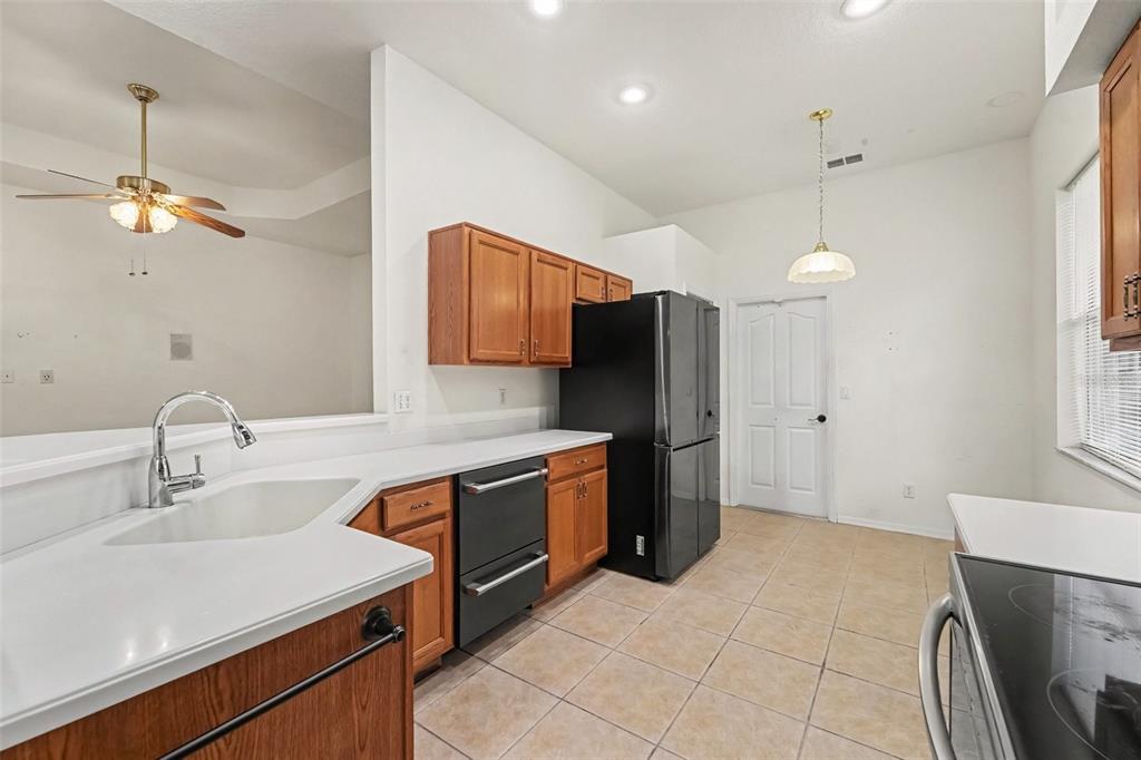 A kitchen features wooden cabinets, white countertops, a black refrigerator, and tile flooring — 48 CACTUS STREET, HOMOSASSA, FL