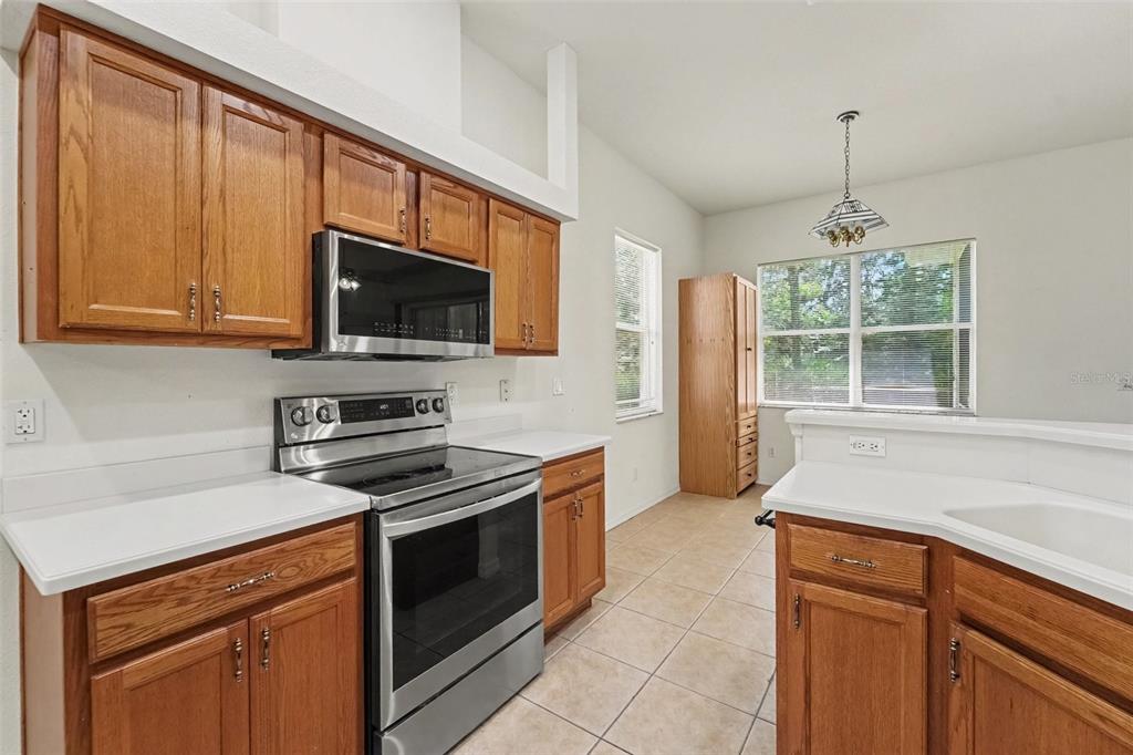 A kitchen with oak cabinets, stainless steel appliances, white countertops, and tile flooring — 48 CACTUS STREET, HOMOSASSA, FL