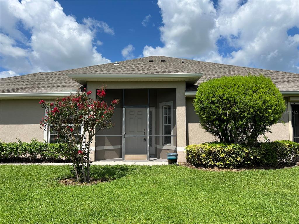 A tan house exterior features a screened-in entryway, a blooming crape myrtle, and manicured landscaping — 3653 LAKEWOOD BOULEVARD, NORTH PORT, FL