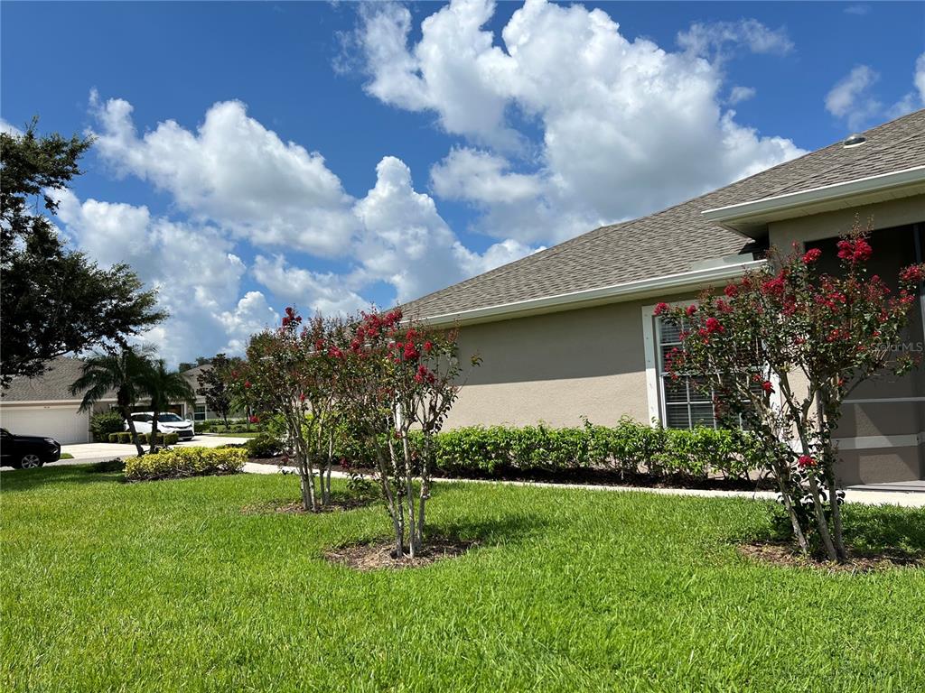 A tan house exterior features a green lawn, red-flowering trees, and a shingled roof — 3653 LAKEWOOD BOULEVARD, NORTH PORT, FL