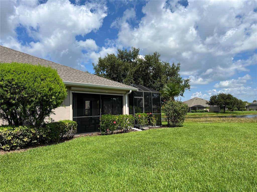 A view of a house exterior with a screened-in patio overlooking a grassy lawn and pond — 3653 LAKEWOOD BOULEVARD, NORTH PORT, FL