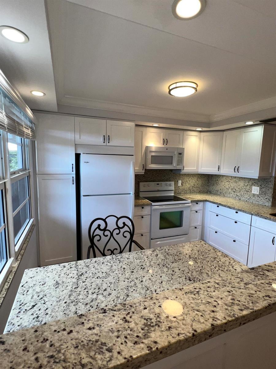 A kitchen features white cabinets, granite countertops, and white appliances under recessed and ceiling lighting — 2202 Lucaya Bend # C4, Coconut Creek FL 33066, COCONUT CREEK, FL