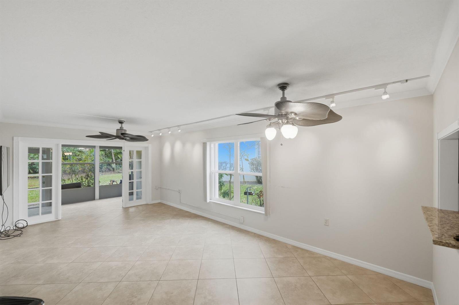 An empty living room with tile floors, two ceiling fans, track lighting, and French doors — 1900 S Kanner Highway # 5107, Stuart FL 34994, STUART, FL