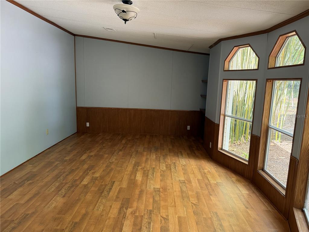 An empty room features wood-look flooring, wood wainscoting, light blue walls, and large windows — 5613 NW 202ND PLACE, LA CROSSE, FL