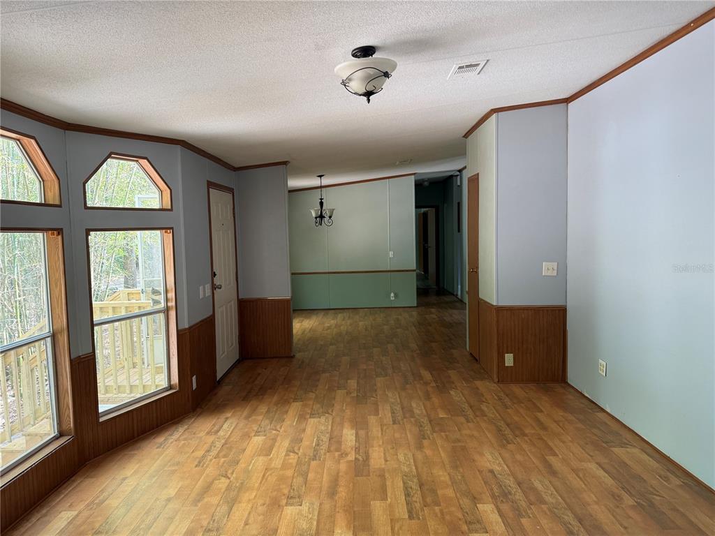 An interior view of a living area featuring wood-look flooring, wainscoting, and large windows — 5613 NW 202ND PLACE, LA CROSSE, FL