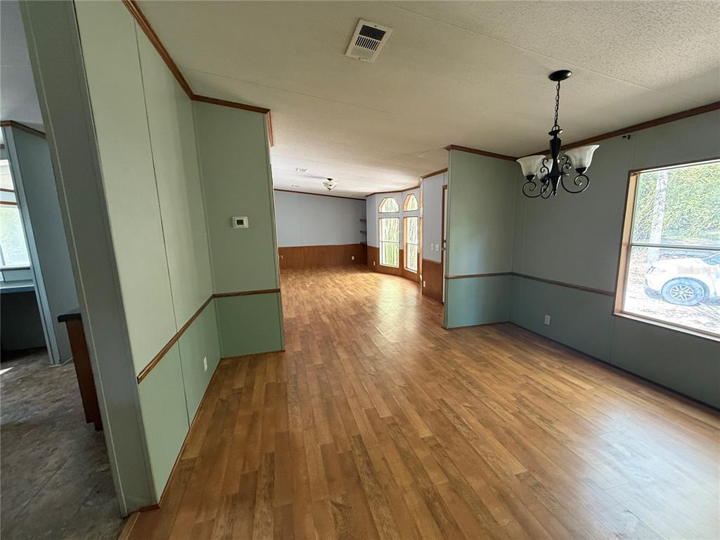 A dining area with wood-look flooring and sage green walls leads into a living room — 5613 NW 202ND PLACE, LA CROSSE, FL
