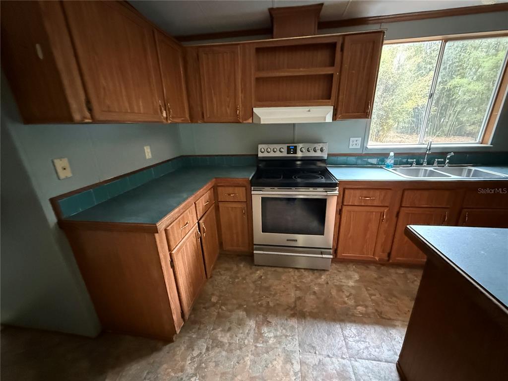 A kitchen features wood cabinets, a stainless steel stove, and teal countertops — 5613 NW 202ND PLACE, LA CROSSE, FL