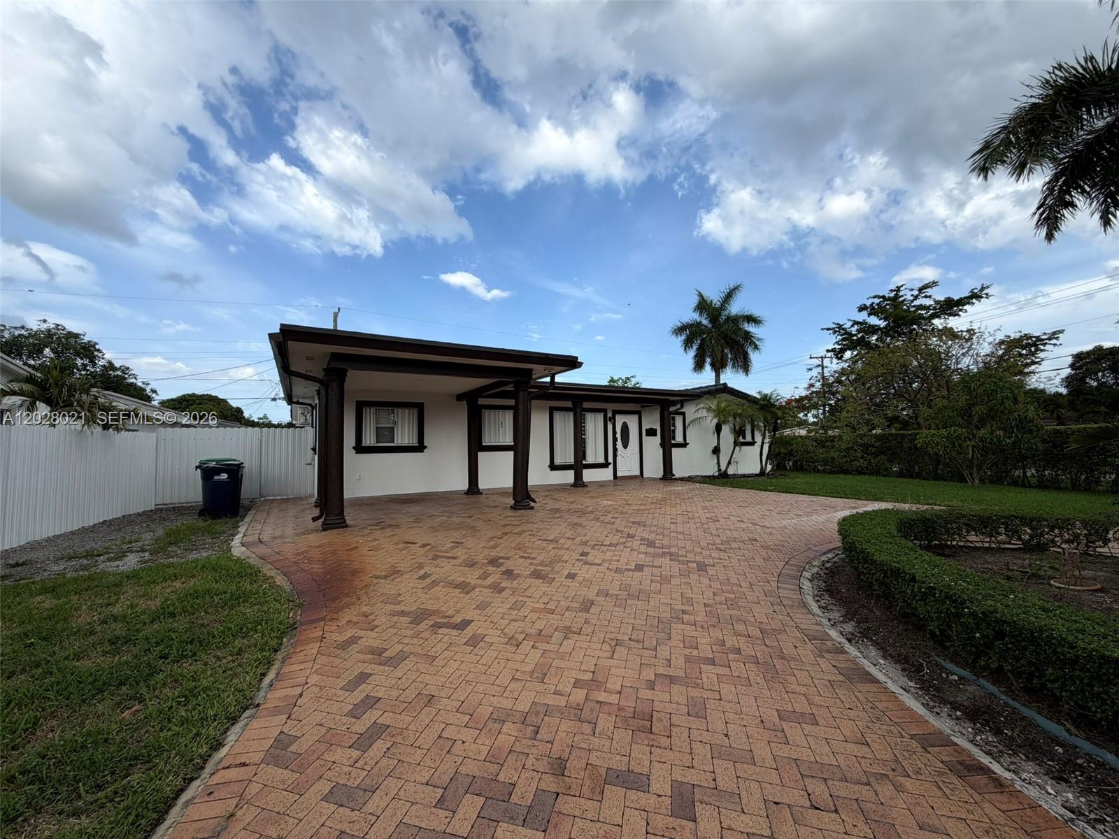 A single-story house features a brick-paved driveway, a covered carport, and a white exterior — MIAMI GARDENS, FL