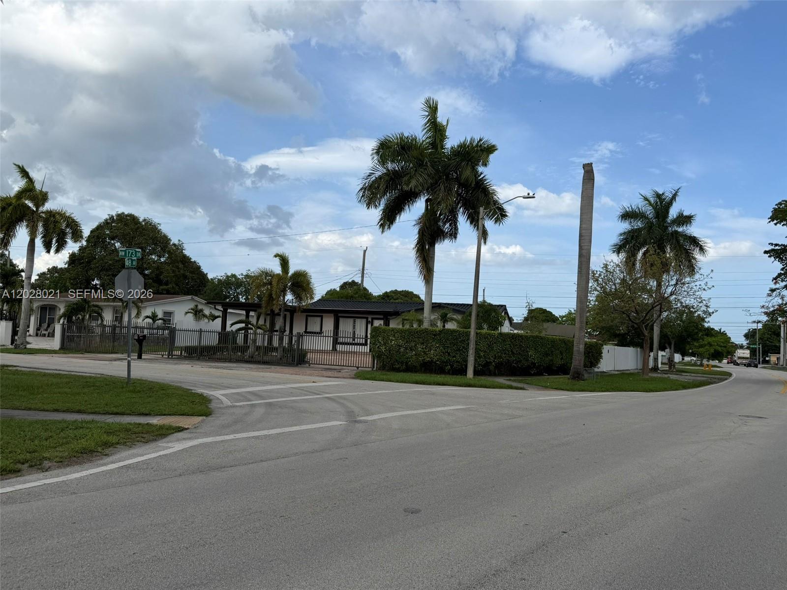 A single-story house with a gated yard and palm trees sits at a street corner — MIAMI GARDENS, FL