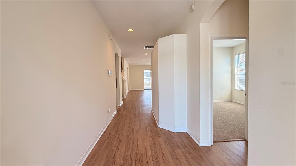 A hallway with wood-look flooring leads toward a bright room with a carpeted floor — 1643 BONITA BLUFF COURT, RUSKIN, FL