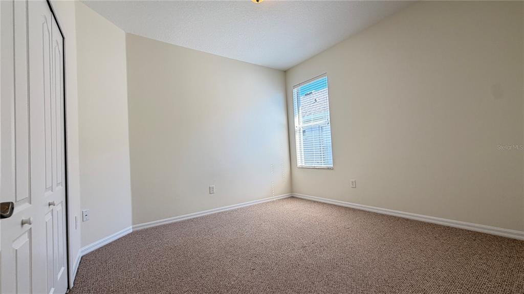 An empty bedroom features beige walls, tan carpeting, a white closet door, and one window — 1643 BONITA BLUFF COURT, RUSKIN, FL