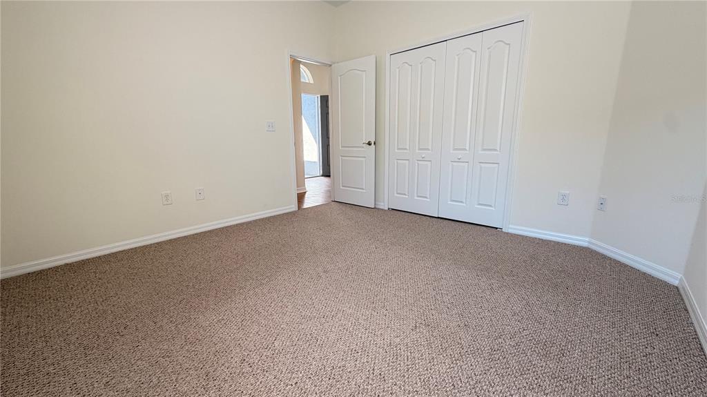 An empty bedroom features beige carpet, white walls, a closet with double doors, and an open doorway — 1643 BONITA BLUFF COURT, RUSKIN, FL