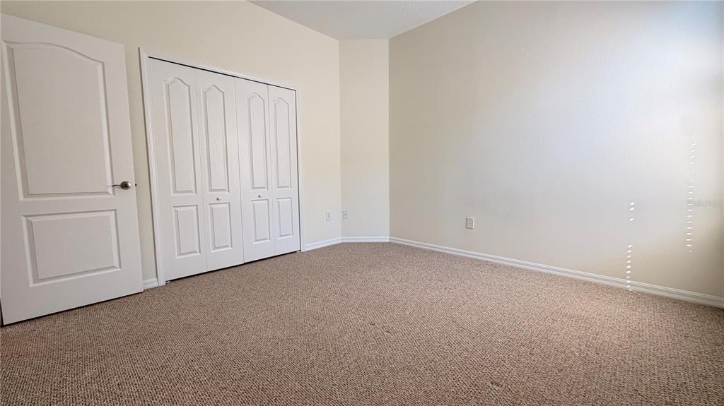 An empty bedroom features beige carpet, white walls, and a white bi-fold closet door — 1643 BONITA BLUFF COURT, RUSKIN, FL