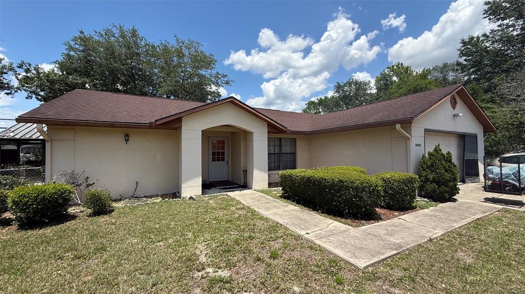 A single-story house with a beige stucco exterior, brown roof, and a concrete walkway — 15165 SW 39TH CIRCLE, OCALA, FL