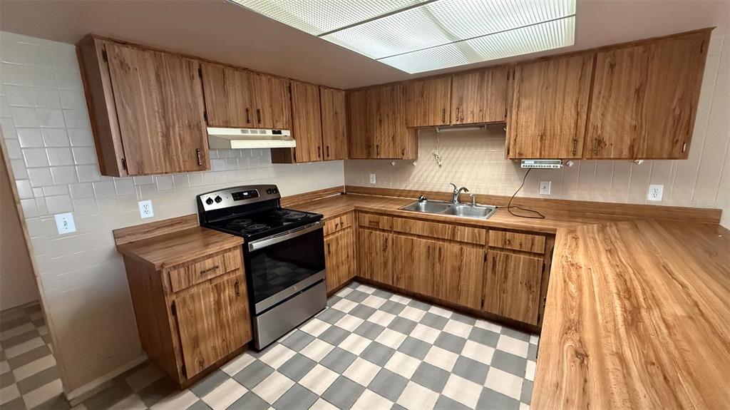 A kitchen features wood-grain cabinets, laminate countertops, a stainless steel stove, and checkered tile flooring — 15165 SW 39TH CIRCLE, OCALA, FL