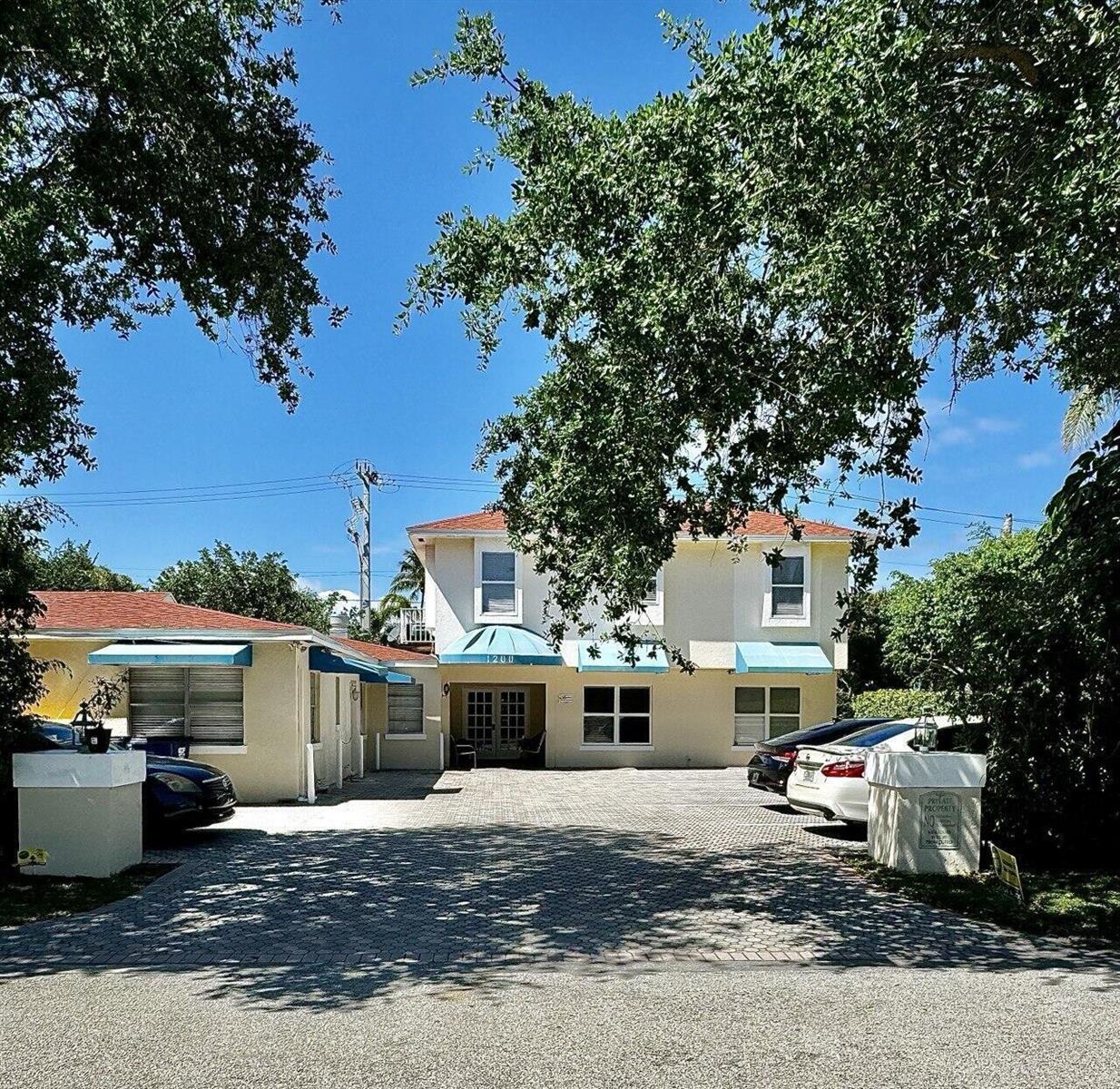 A two-story building with light-colored stucco walls, blue awnings, and a paved parking area — 1200 Surf Road, Singer Island FL 33404, SINGER ISLAND, FL