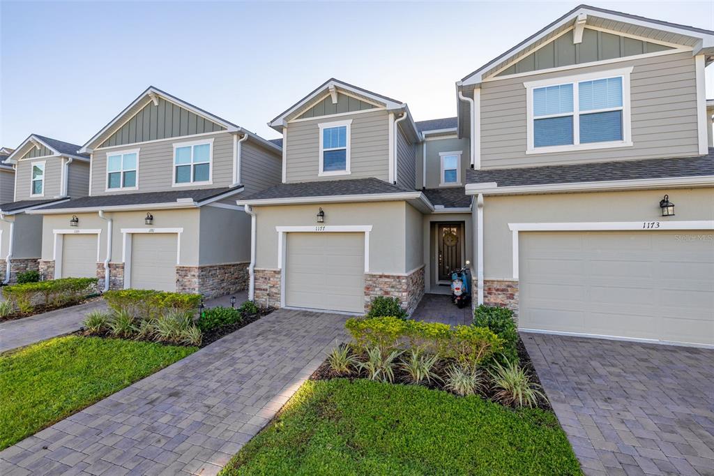 A row of three-story townhomes with beige siding, stone accents, and paved driveways — 1177 SEASIDE MIST TRAIL, KISSIMMEE, FL