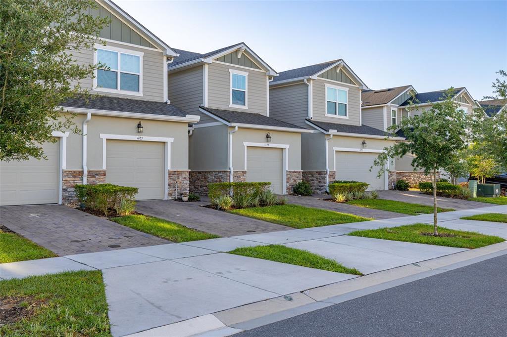 A row of multi-story townhomes with beige siding, stone accents, and attached garages — 1177 SEASIDE MIST TRAIL, KISSIMMEE, FL