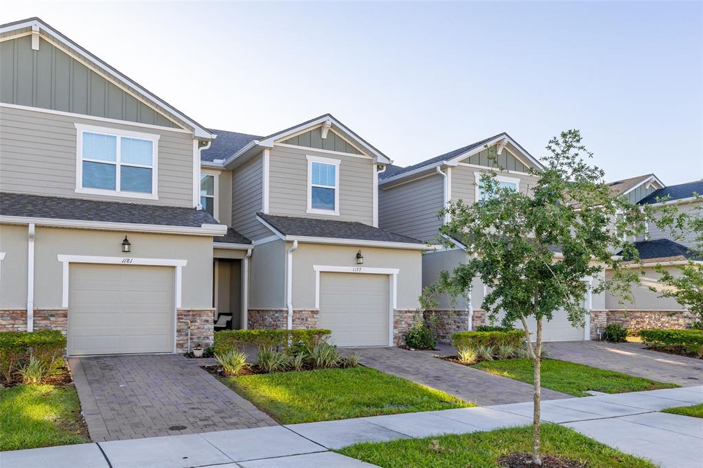 A row of two-story townhomes with beige siding, stone accents, and attached garages — 1177 SEASIDE MIST TRAIL, KISSIMMEE, FL