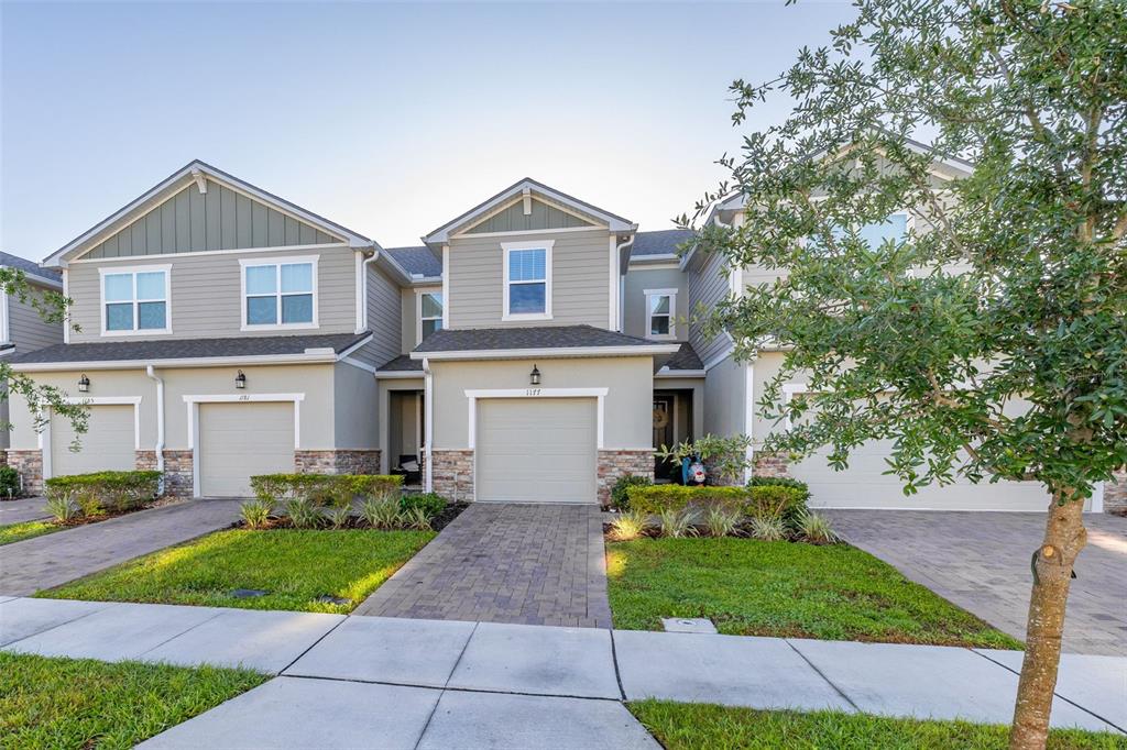 A row of three attached townhomes with beige siding, stone accents, and paved driveways — 1177 SEASIDE MIST TRAIL, KISSIMMEE, FL