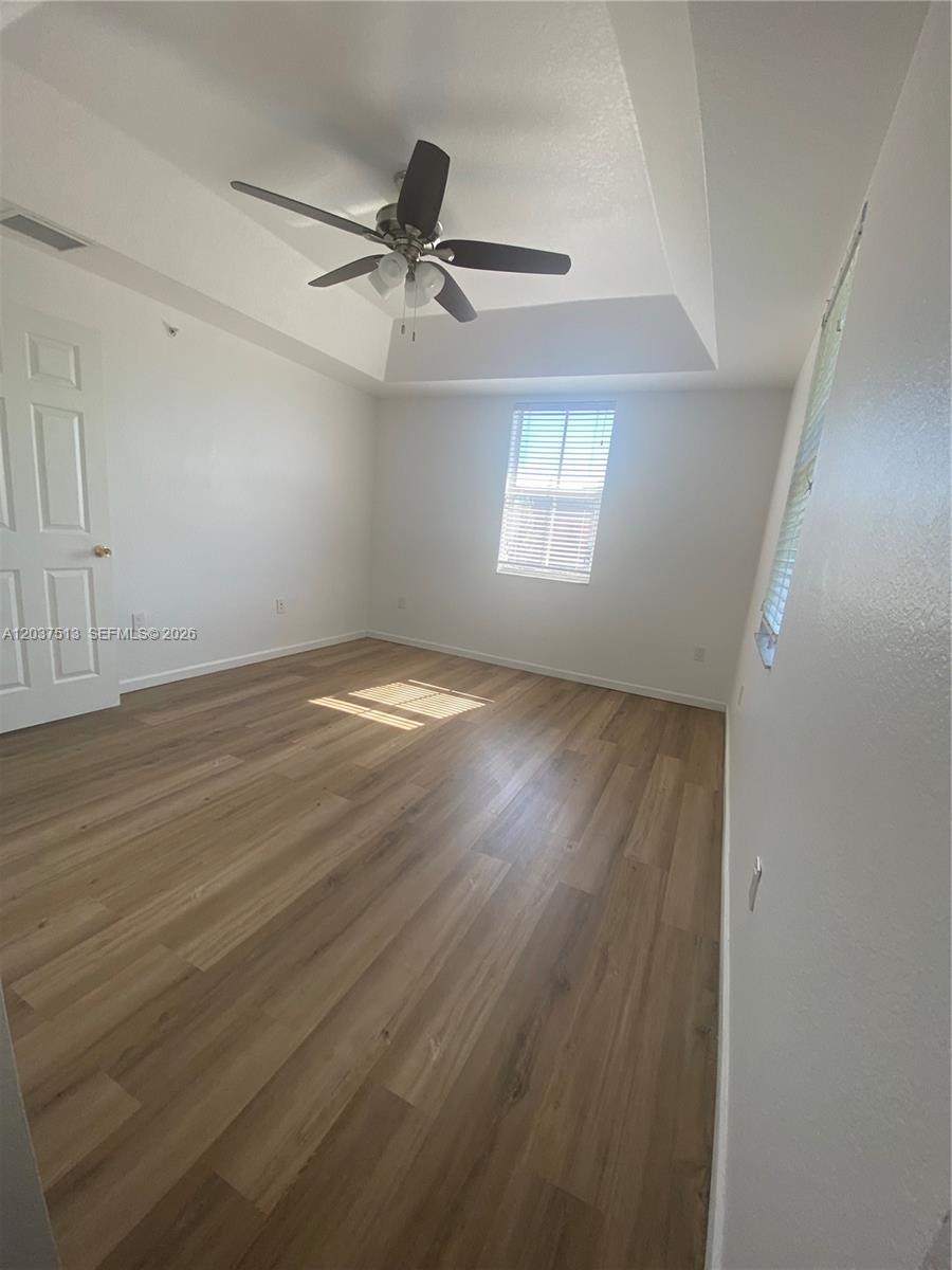 An empty bedroom features light wood-look flooring, a tray ceiling with a fan, and windows — 11103 NW 83rd St # 201, Doral FL 33178, DORAL, FL