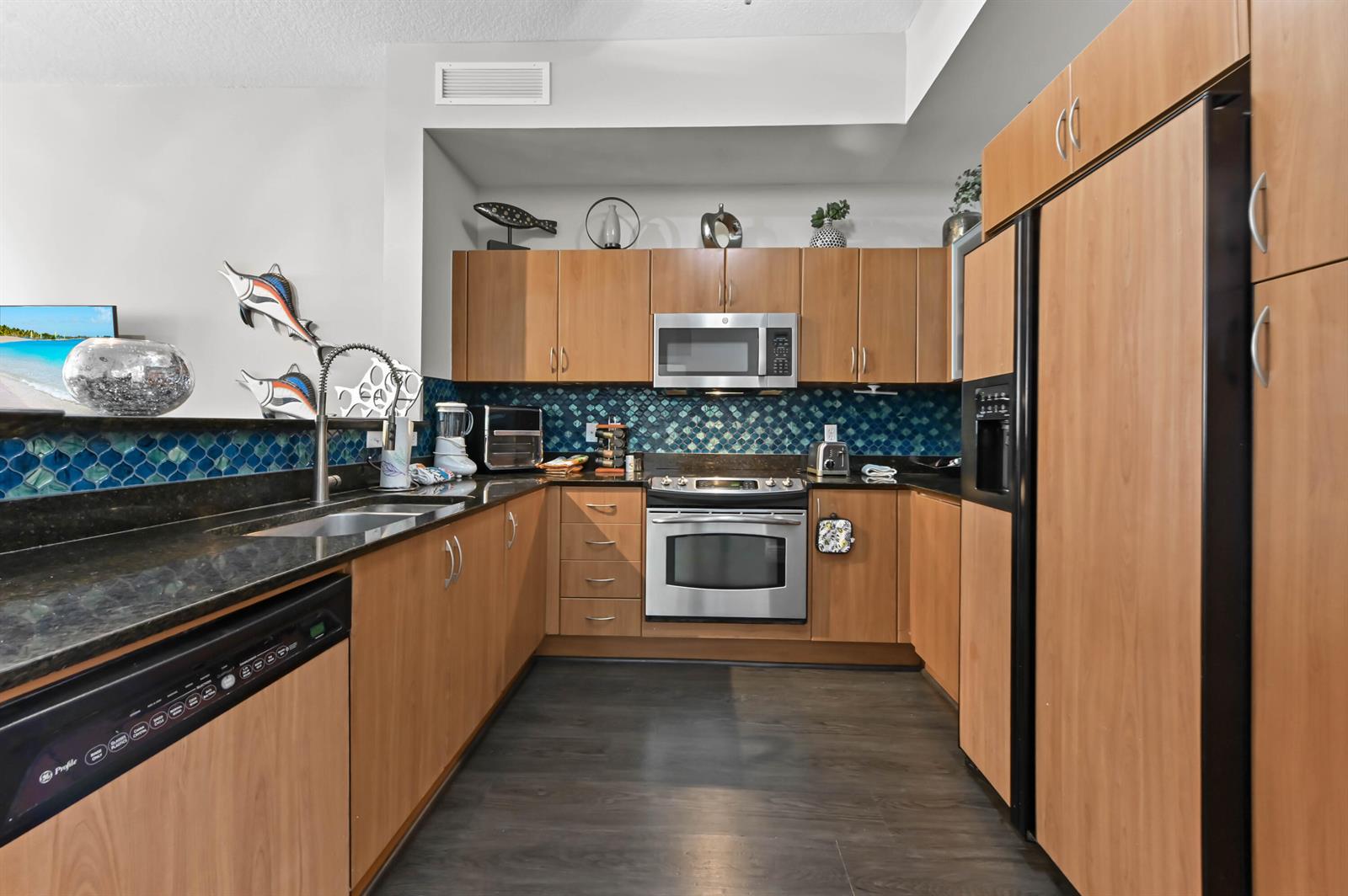 A kitchen features wood cabinets, stainless steel appliances, dark countertops, and a blue tiled backsplash — 804 E Windward Way # 120, Lantana FL 33462, LANTANA, FL