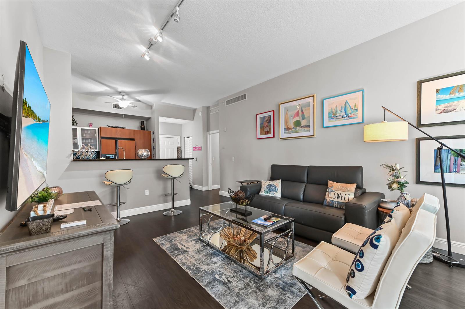 A living room with dark wood floors, a gray sofa, and an open kitchen area — 804 E Windward Way # 120, Lantana FL 33462, LANTANA, FL