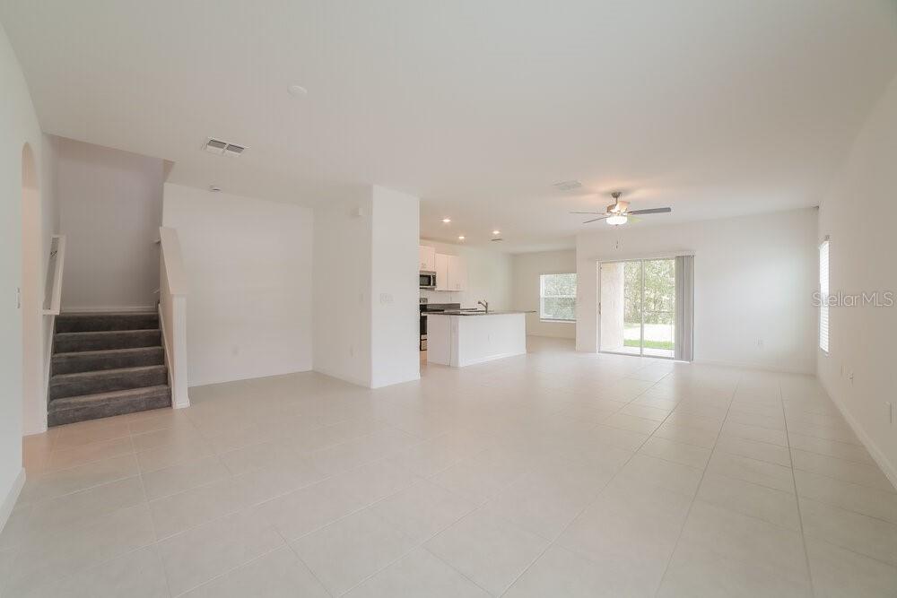 An open-concept living area features a carpeted staircase, tile flooring, and a kitchen with white cabinets — 7230 SPRING SNOWFLAKE AVENUE, TAMPA, FL