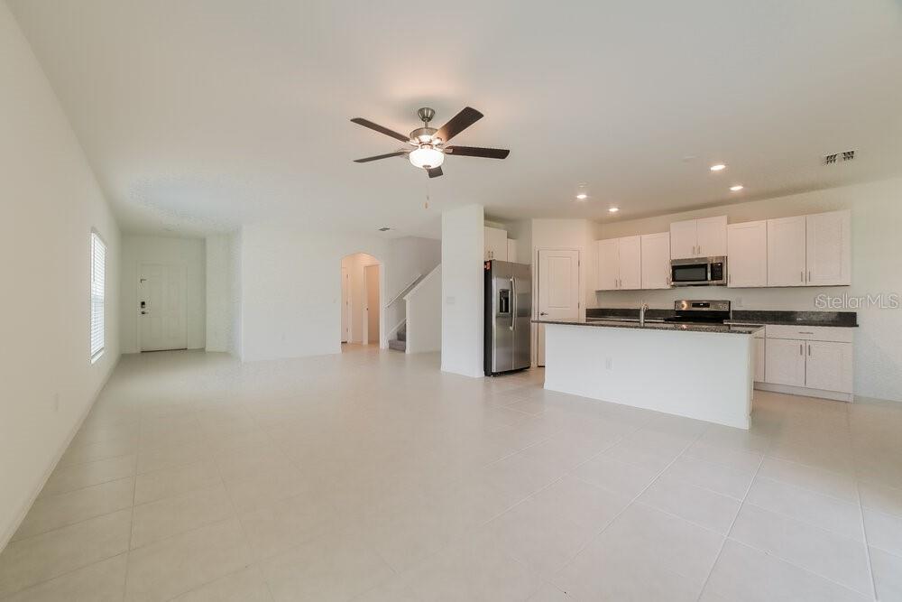 An open-concept kitchen and living area features white cabinetry, stainless steel appliances, and tile flooring — 7230 SPRING SNOWFLAKE AVENUE, TAMPA, FL