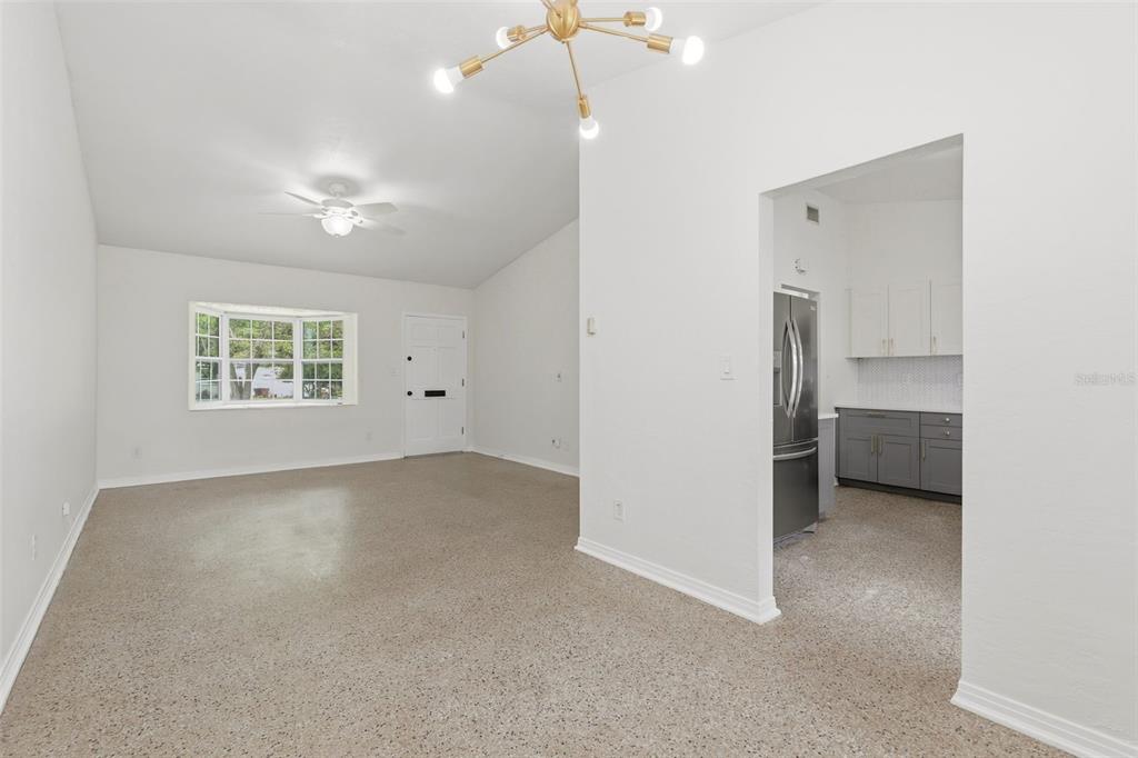 An empty living room features white walls, a vaulted ceiling, and speckled concrete flooring — 724 BRAIDWOOD LANE, ORLANDO, FL