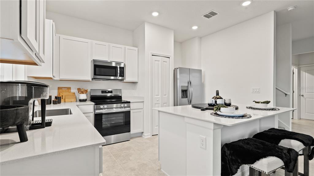 A modern kitchen features white cabinets, stainless steel appliances, a center island, and tile flooring — 5795 ENERGY WAY, CLERMONT, FL