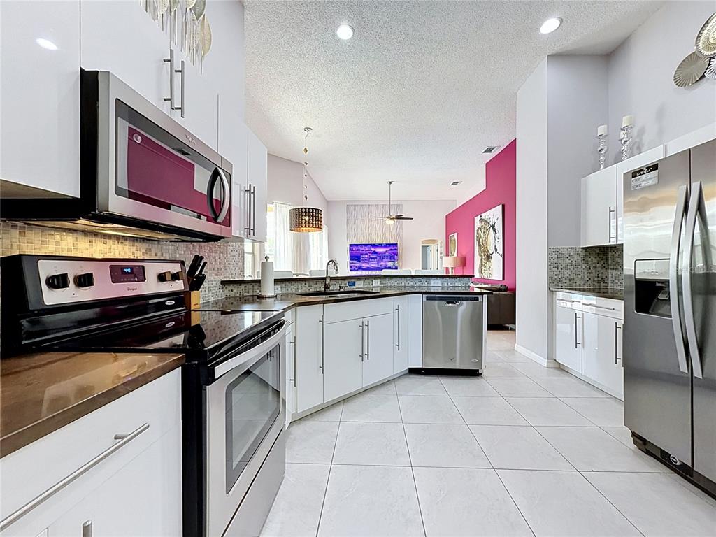 A modern kitchen features white cabinets, stainless steel appliances, and a view into the living area — 844 MONTANA AVENUE, DAVENPORT, FL