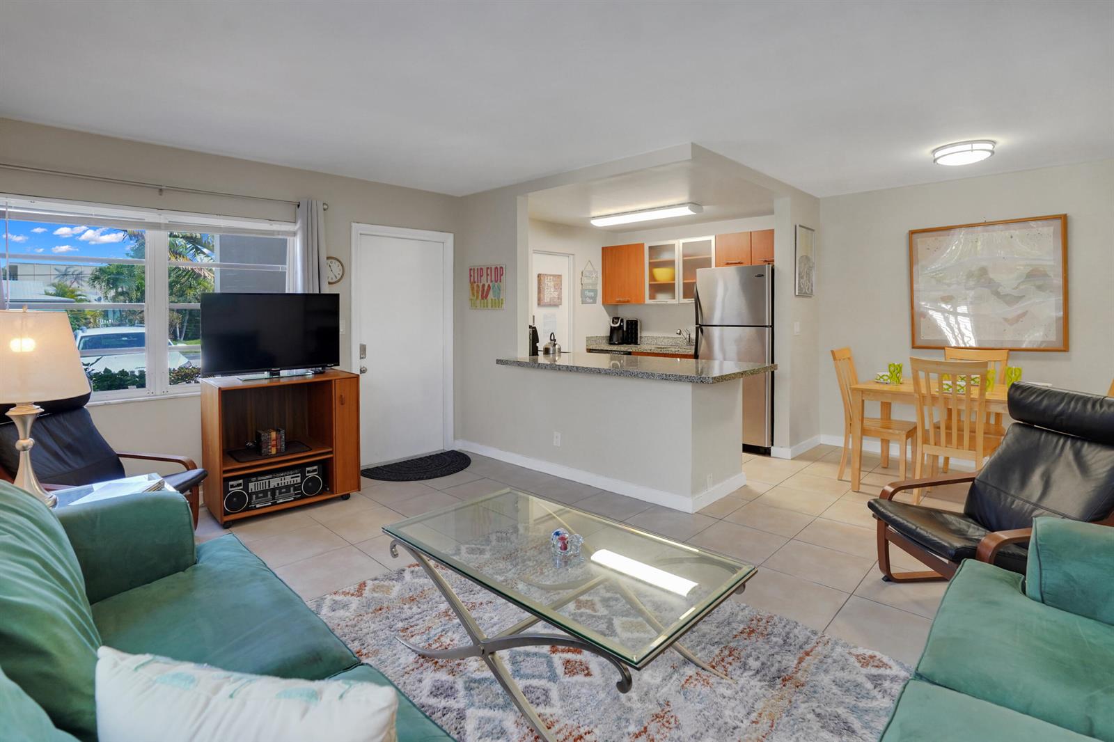 A living room with a glass coffee table, green sofa, and an open kitchen area — 3212 NE 9th # A104, Pompano Beach FL 33062, POMPANO BEACH, FL