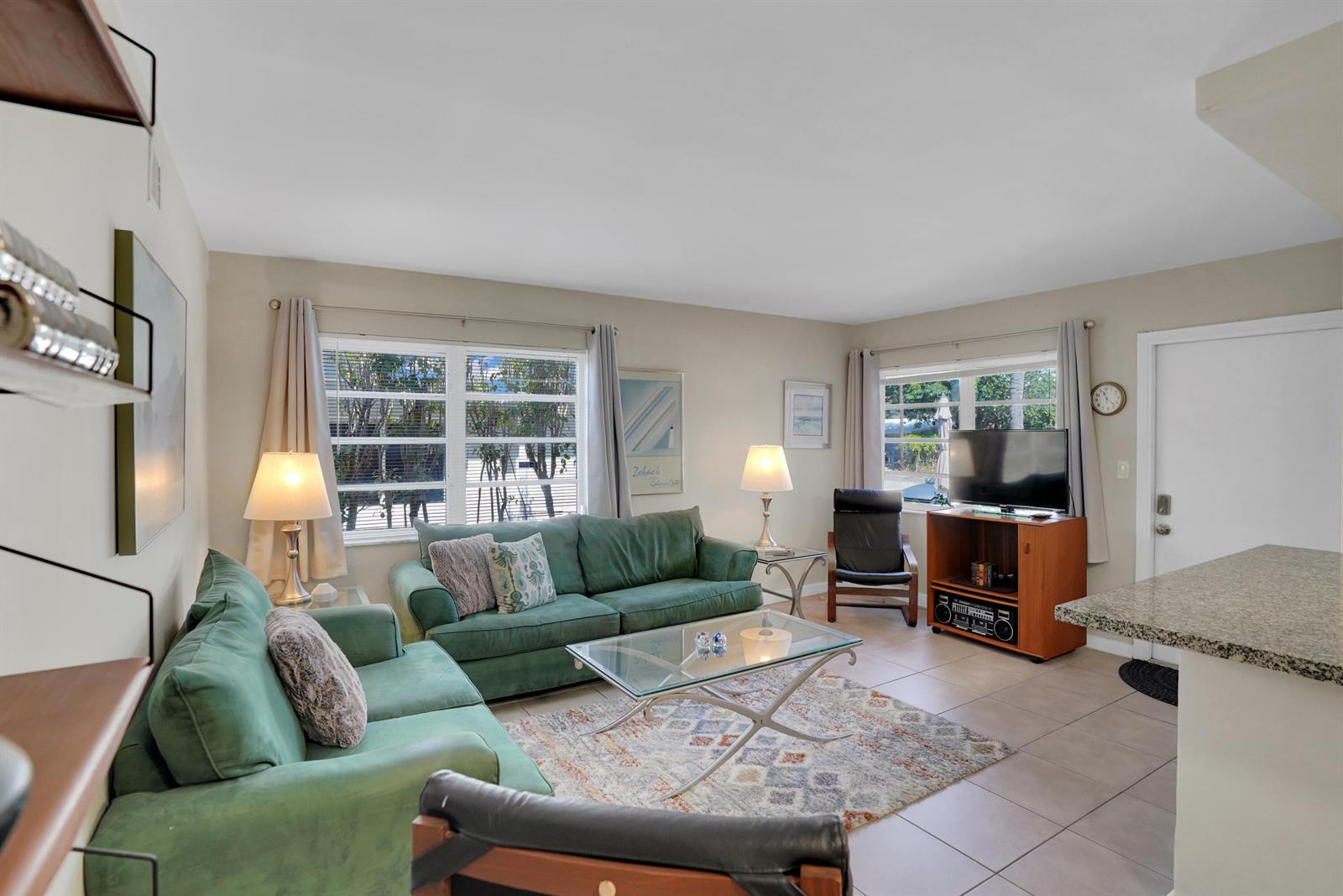 A living room features green sofas, a glass coffee table, and tile flooring — 3212 NE 9th # A104, Pompano Beach FL 33062, POMPANO BEACH, FL