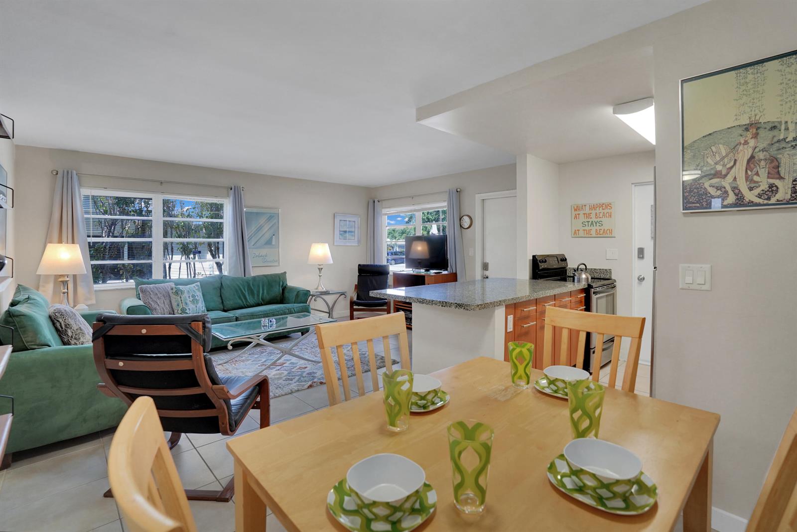 An open-concept living and dining area features a green sofa, kitchen island, and wooden table — 3212 NE 9th # A104, Pompano Beach FL 33062, POMPANO BEACH, FL