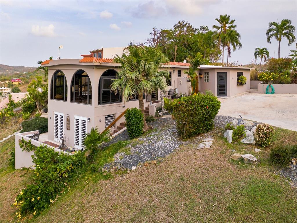 An exterior view of a tan house with arched windows and a sloped grassy yard — 397 CASA EGRETTA, VIEQUES, PR