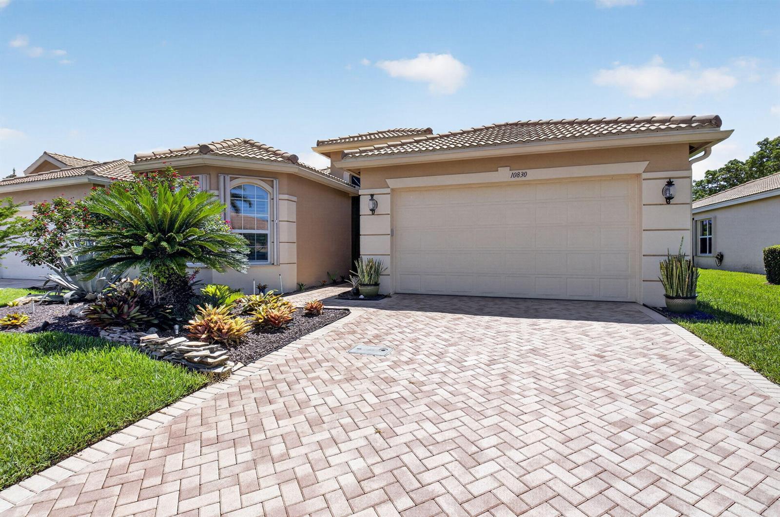 A beige house features a paved driveway, a two-car garage, and a landscaped front yard — 10830 Leaf Bridge Way, Boynton Beach FL 33473, BOYNTON BEACH, FL