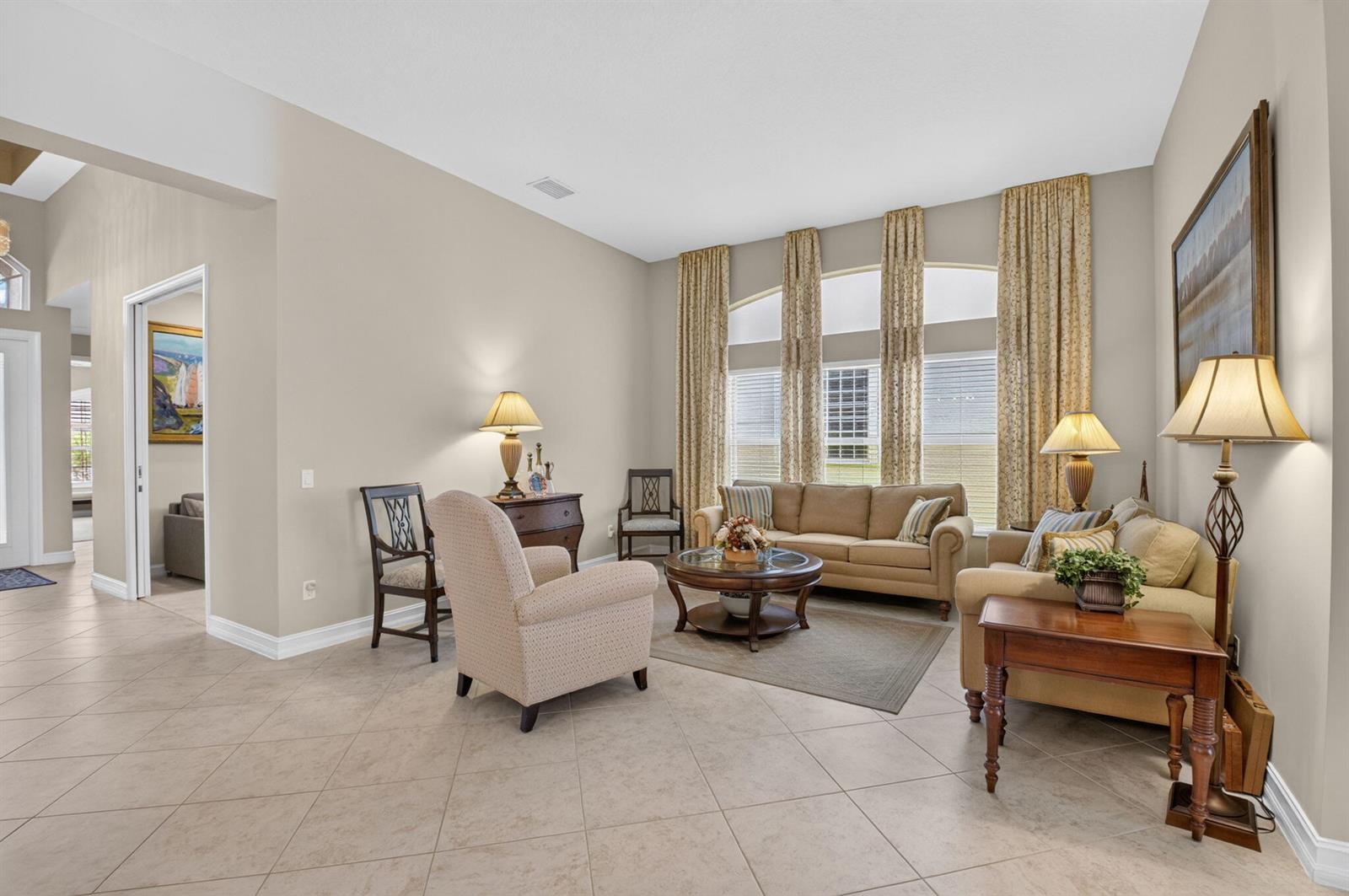 A living room features beige tile floors, neutral walls, two sofas, and tall arched windows — 10830 Leaf Bridge Way, Boynton Beach FL 33473, BOYNTON BEACH, FL