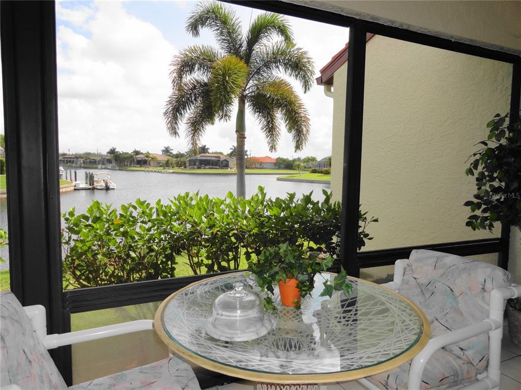 A screened-in patio features a glass-topped table and chairs overlooking a canal and palm tree — 3830 BAL HARBOR BOULEVARD UNIT 12, PUNTA GORDA, FL