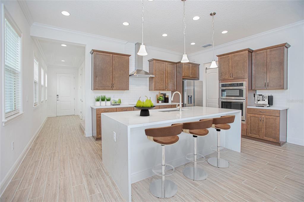 A modern kitchen features wood cabinets, a white quartz island with stools, and tile flooring — 13300 BROMBOROUGH DRIVE, ORLANDO, FL