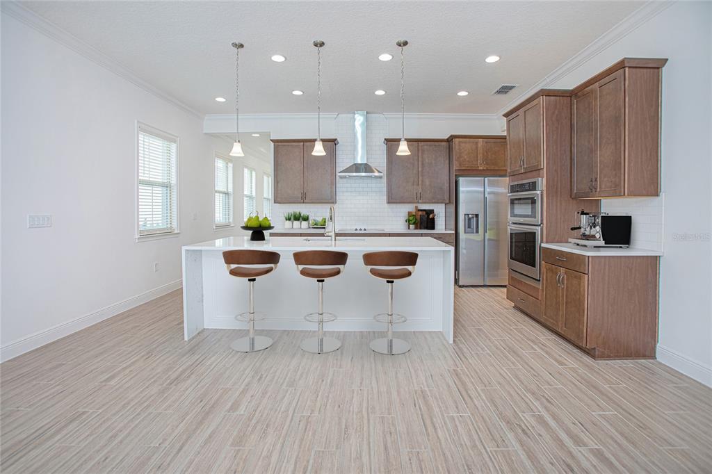 A modern kitchen features a white island with three stools, wood cabinets, and tile flooring — 13300 BROMBOROUGH DRIVE, ORLANDO, FL