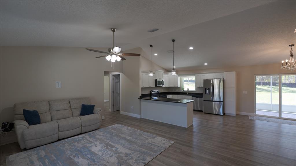 An open-concept living room and kitchen featuring light wood flooring, white cabinets, and stainless appliances — 6374 W RIO GRANDE DRIVE, BEVERLY HILLS, FL