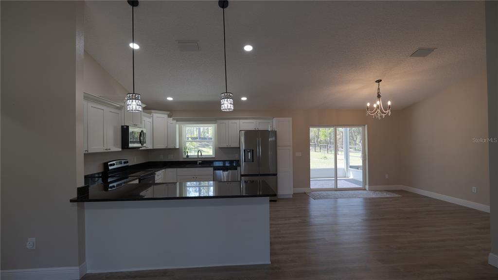 A kitchen with white cabinets, black countertops, and stainless steel appliances opens to a living area — 6374 W RIO GRANDE DRIVE, BEVERLY HILLS, FL