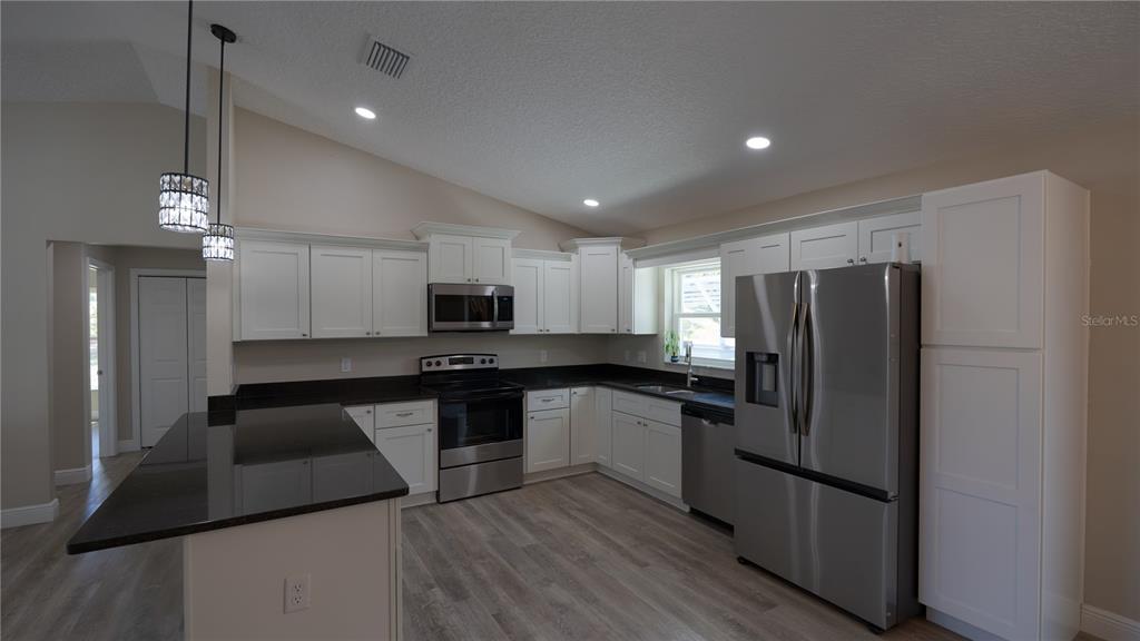 A kitchen features white cabinets, black countertops, stainless steel appliances, and light wood-look flooring — 6374 W RIO GRANDE DRIVE, BEVERLY HILLS, FL